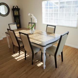 A modern dining room with a wooden table and six chairs, illuminated by natural light from a window.
