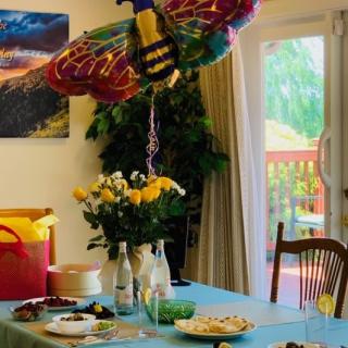 A festive indoor party setup with a colorful balloon decoration and a table set with food and flowers.