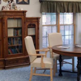 A cozy library room with bookshelves, chairs, and a table near the window.