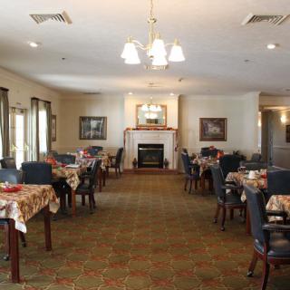 A well-lit dining room with tables and chairs arranged around a central fireplace.