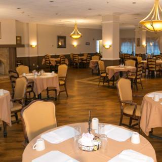 An elegant restaurant dining room with neatly arranged tables and chairs, featuring warm lighting from chandeliers.