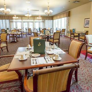 A formal dining room with neatly arranged tables and chairs, featuring elegant chandeliers.