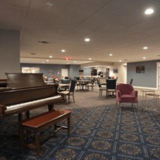 A spacious room with a piano and various seating arrangements, featuring a patterned carpet and warm lighting.
