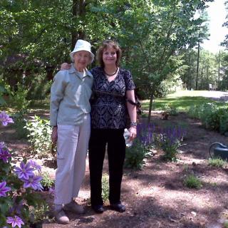 Two people standing together in a garden surrounded by greenery and flowers.