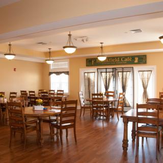 An empty dining room with wooden tables and chairs, set under soft lighting.