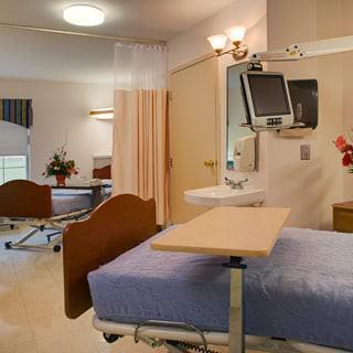 A clean and well-equipped hospital room featuring a medical bed, television, and privacy curtain.