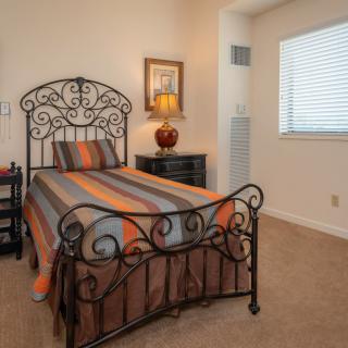 A cozy bedroom featuring a single bed with decorative metal frame, a nightstand with a lamp, and a window with blinds.
