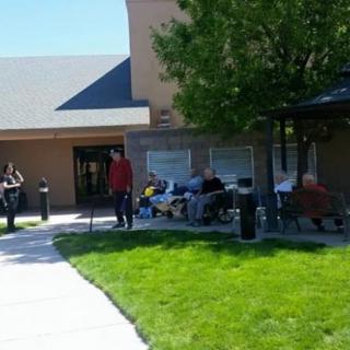 A group of people enjoying a sunny day outside near a building with a green lawn.