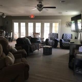A cozy living room with sofas, chairs, and a TV, illuminated by natural light from large windows.