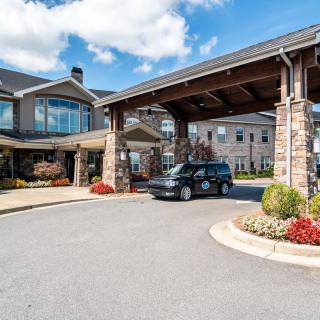 A van parked under a covered entrance at a large building with stone pillars and landscaped surroundings.