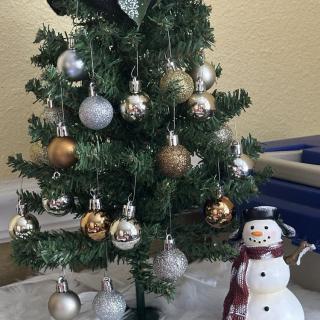A small decorated Christmas tree with gold and silver ornaments stands next to a snowman figure.