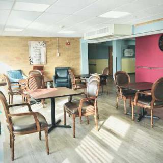 An empty cafe with wooden floors, tables, and chairs illuminated by daylight.