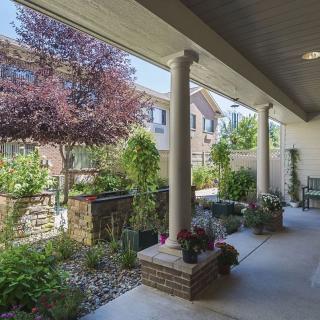 A serene patio area with columns, surrounded by lush plants and a garden.
