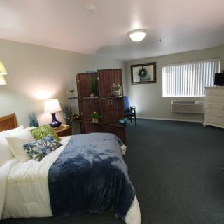 A spacious bedroom with a neatly made bed, a dresser, and a partition dividing the room.