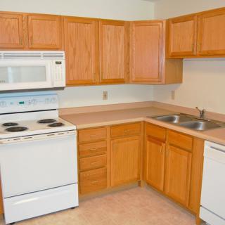 A kitchen featuring wooden cabinets, a white stove, microwave, sink, and dishwasher.
