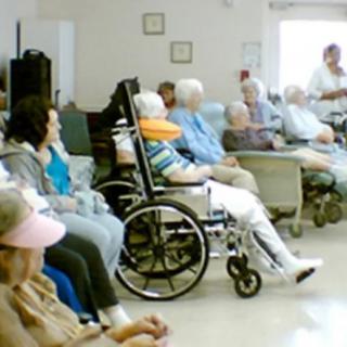 A group of elderly individuals in a nursing home setting, seated in wheelchairs and chairs.