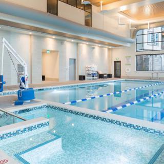 A modern indoor swimming pool with designated lanes and a pool lift, featuring large windows and bright lighting.