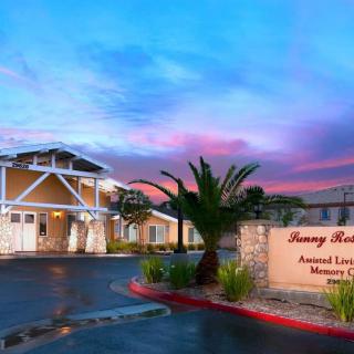 A view of a memory care and assisted living facility at sunset, featuring a palm tree and vibrant sky.