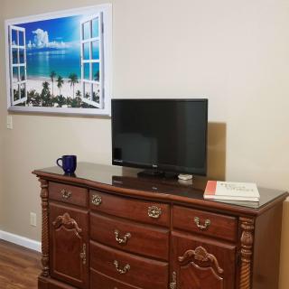 A room with a wooden dresser, a small television on top, and a framed artwork of a beach scene on the wall.