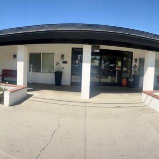The image shows the exterior entrance of a building with glass doors and a paved area.