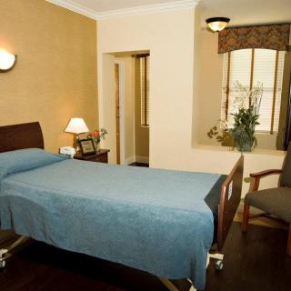 A hospital room featuring a bed with a blue cover, a chair, and a window with curtains.