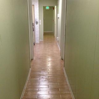 A long hallway with green walls and tiled flooring, lined with doors on either side.