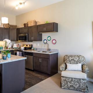 A modern open-space kitchen with dark cabinetry, a kitchen island, and a cozy armchair.