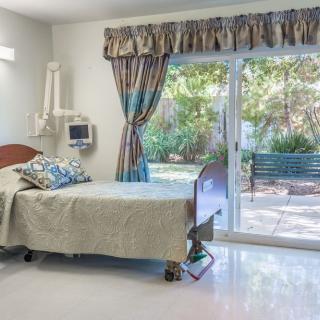 A bright hospital room with a patient bed and a view of the garden outside.