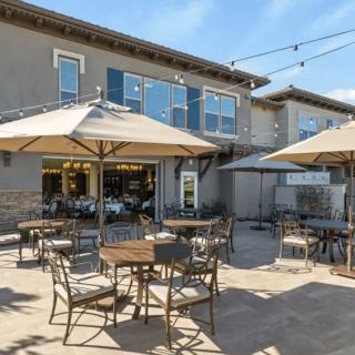 An outdoor cafe patio with tables, chairs, and umbrellas set up for customers on a sunny day.