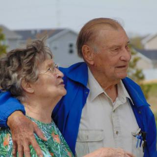 An elderly couple enjoying a moment outdoors, embracing each other warmly.