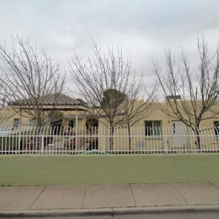 A building with a white fence and leafless trees on a cloudy day.