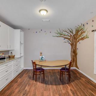 A modern kitchen with a dining area featuring a tree mural on the wall and wooden flooring.