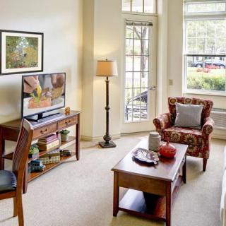 A cozy living room with a television, chair, lamp, and coffee table by a large window.