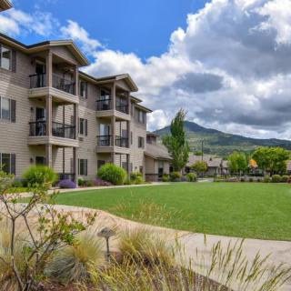 A modern apartment building overlooks a well-maintained grassy lawn with scenic mountain views under a cloudy sky.