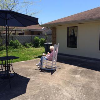 A person sits in a rocking chair on a sunny patio.