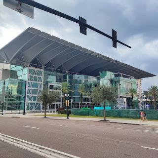 A modern glass building under a cloudy sky, with construction barriers in the foreground.
