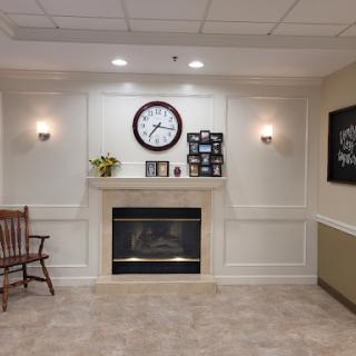 A cozy living room setting with a fireplace, wall clock, and pictures adorning the walls.