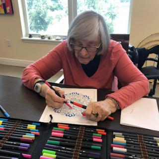 A senior woman engages in a creative coloring activity, surrounded by an array of colorful markers.