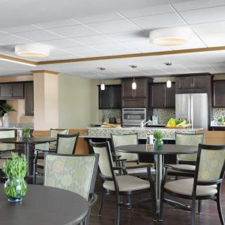 A modern dining area with tables and chairs adjacent to a kitchen, featuring sleek appliances and contemporary lighting.