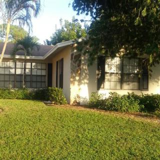 A cozy residential house with a well-maintained lawn and surrounding trees basking in sunlight.