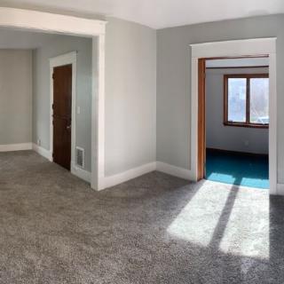 A bright, carpeted living room with sunlight streaming through the windows.