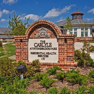 A decorative brick sign with a building in the background, surrounded by landscaping.