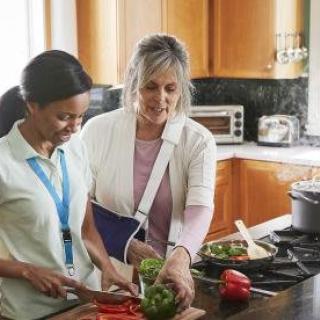 A person with their arm in a sling receives help with cooking in the kitchen.