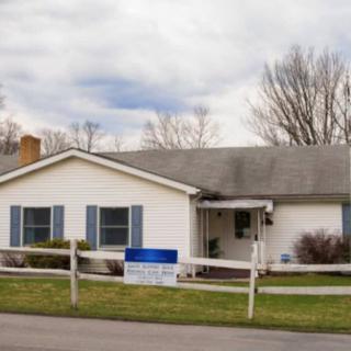 A single-story residential house with a white exterior and blue shutters, surrounded by a wooden fence, under a cloudy sky.