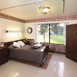 A cozy and well-lit bedroom with a simple design, featuring a bed, nightstand, and large window offering a view of the outdoors.