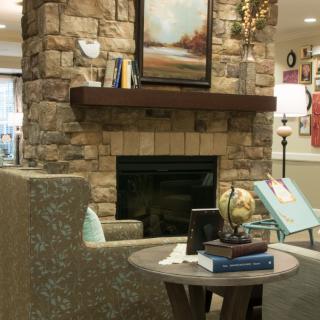 A cozy living room with a stone fireplace, adorned with books and a painting above the mantel.