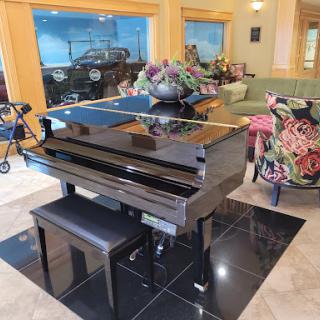 A polished black piano in a stylish living space, surrounded by elegant furniture and floral decor.