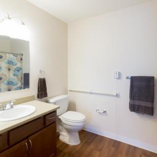 A clean and simple bathroom interior with a sink, toilet, and wooden flooring.