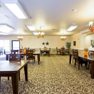 A spacious dining room with wooden tables and chairs, featuring patterned carpeting and bright lighting.