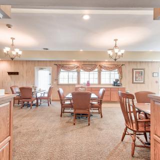 A spacious dining room with multiple tables and chairs, featuring chandeliers and natural lighting from large windows.